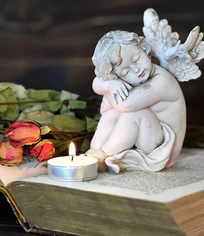 angel statue with lighted candle on top of book